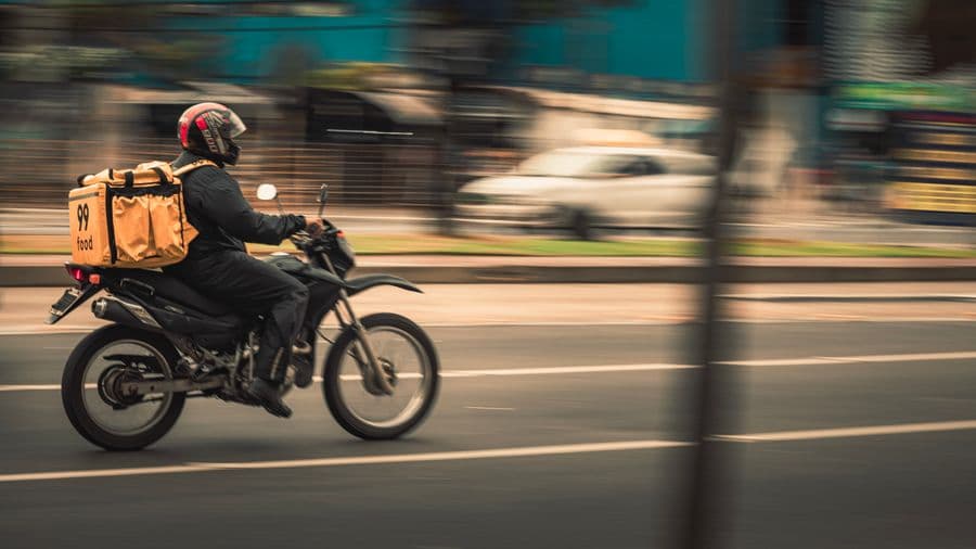 A motorcycle courier riding through traffic with a delivery box mounted behind the rider.
